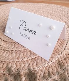 a place card sitting on top of a woven table cloth with pearls attached to it