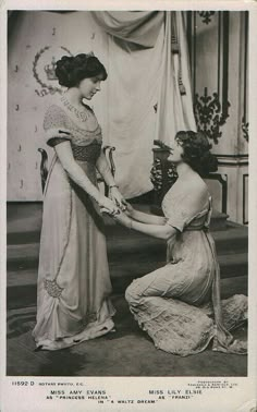 an old black and white photo of two women in formal dress, one holding the other's hand