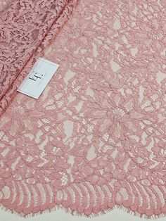 a pink lace fabric with small flowers on the side and a tag attached to it