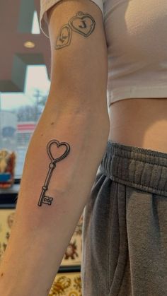 a woman with a tattoo on her arm holding a key to the heart shaped lock