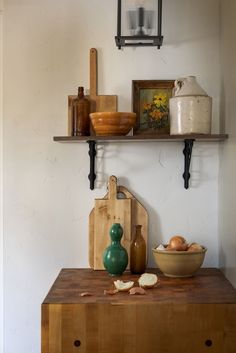 a wooden table topped with bowls and cutting boards next to a shelf filled with utensils