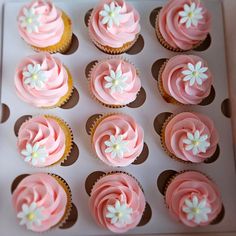 cupcakes with pink frosting and white flowers on them are arranged in a box