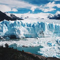 a large glacier with lots of ice on the water and mountains in the background,