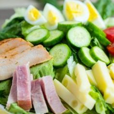 a salad with ham, cheese and cucumbers in it on a white plate