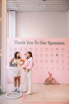 two women standing next to each other in front of a pink sign that says thank you to our sponsors