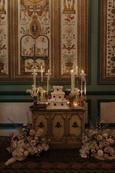 a wedding cake sitting on top of a table next to some flowers and lit candles