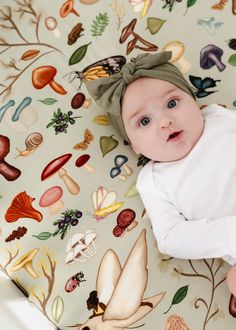 a baby laying on top of a bed covered in lots of different types of mushrooms