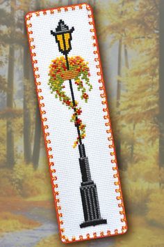 a cross - stitch bookmark with a lamp post and flowers on it in the fall