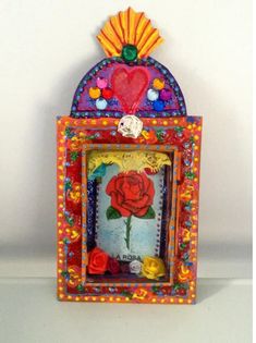 a small colorful box with a red rose in the center and other decorations around it