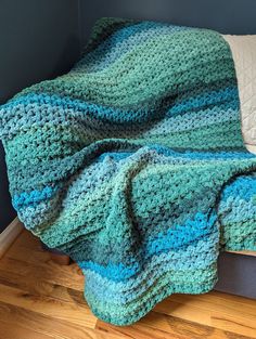 a blue and green crocheted blanket sitting on top of a bed next to a pillow