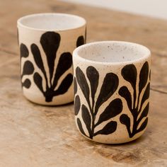 two black and white cups sitting on top of a wooden table