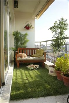 a balcony with green grass and potted plants on the floor, next to a wooden bench