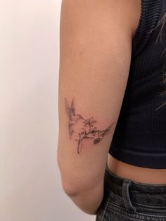 a woman's arm with a small bird and flowers tattoo on the left shoulder