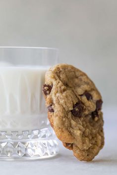 an oatmeal cookie next to a glass of milk on a white surface