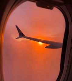 an airplane window with the sun setting in the sky as seen through it's wing