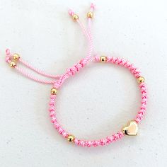 a pink and gold bracelet with a heart charm on the end, sitting on a white surface