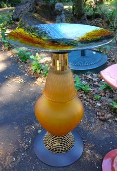 an upside down glass table sitting in the middle of a park with trees and bushes behind it