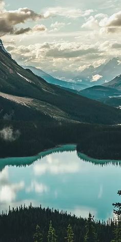 a lake surrounded by mountains with clouds in the sky