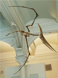 a large metal spider sculpture hanging from the ceiling in a room with white walls and columns