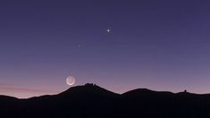 the moon and venus are visible in the night sky over some mountain tops, as seen from afar