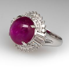 This spectacular ballerina ring is centered with one (1) oval cabochon cut star ruby set into a four-prong setting. The ruby is surrounded by thirty-eight (38) prong set round brilliant cut diamonds and ten (10) prong set tapered baguette cut diamonds. The ring measures 17.4mm at the top, rises 13.1mm above the finger, tapering to 2.9mm wide and 1.2mm thick at the base of the shank. It is currently a size 5.25. The ruby has a few surface reaching inclusions but this is common for the stone and does not take away from its beauty at all. Luxury Ruby Cabochon Diamond Ring, Fine Jewelry Cabochon Ruby Ring In White Gold, Fine Jewelry White Gold Cabochon Ruby Ring, Fine Jewelry Ruby Cabochon Ring In White Gold, Fine Jewelry White Gold Ruby Ring With Cabochon, Oval Cabochon Ruby Ring With Diamonds, Fine Jewelry Ruby Cabochon Ring, Formal Ruby Ring With Diamond And Oval Cabochon Shape, Formal Oval Cabochon Ruby Ring With Diamond