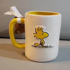 a yellow and white coffee mug with a cartoon character on the side, sitting on a table