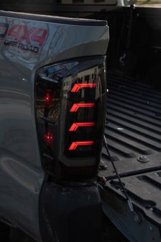 the tail lights of a silver truck with red lettering on it's bumpers