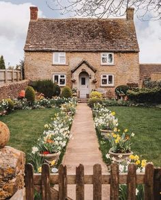 a brick house with flowers in the front yard and a wooden fence around it that leads to an entry way