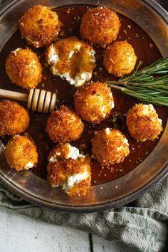 some food is in a metal bowl with a wooden spoon and rosemary sprig