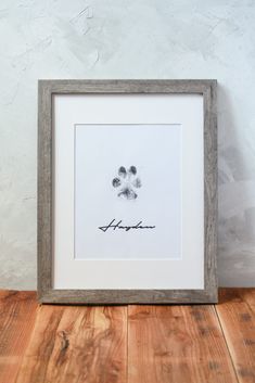 a dog's paw print is displayed in a frame on a wooden floor next to a wall