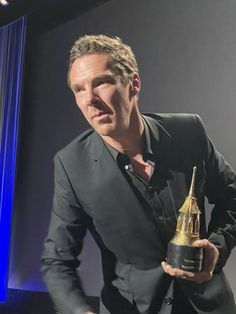 a man in a black suit holding a golden trophy and posing for the camera with his hands on his hips