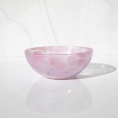 a pink glass bowl sitting on top of a white table next to a light colored wall