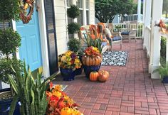 the front porch is decorated for fall with pumpkins and other flowers in blue pots