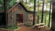 a small cabin in the woods with picnic table and benches around it's perimeter