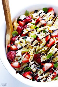 a white bowl filled with pasta, strawberries and chocolate sauce next to a wooden spoon