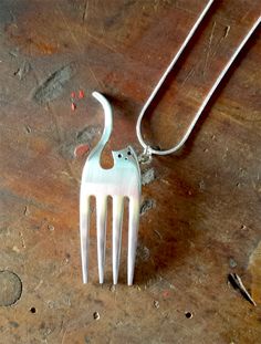 a white cat shaped fork is sitting on a wooden table next to a silver necklace