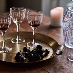 wine glasses and some black grapes on a gold platter with candles in the background