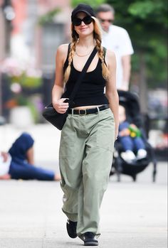 a woman walking down the street wearing green pants and a black tank top with braids