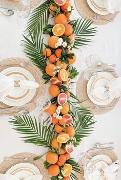 an arrangement of oranges and other fruits on a table with plates, napkins and utensils