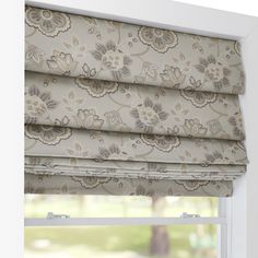 an open window with roman blinds and floral print on the valance, in front of a white wall