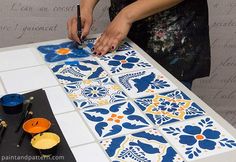 a person is painting on a tile with blue and orange designs in front of them