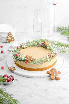 a cake decorated with greenery and gingerbreads on a white platter surrounded by christmas decorations