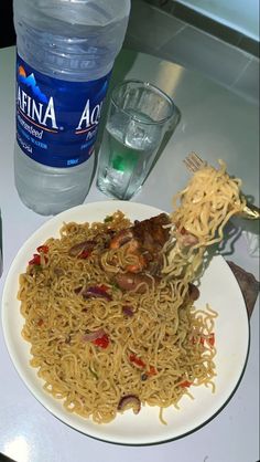 a white plate topped with noodles and meat on top of a table next to a bottle of water