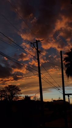 the sun is setting behind power lines and telephone poles with palm trees in the background