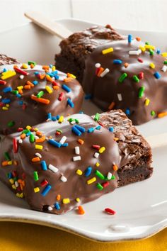 brownies on a stick with chocolate frosting and sprinkles are sitting on a plate