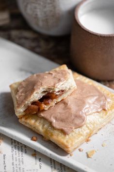 a pastry with chocolate frosting on it sitting on top of a table next to a cup