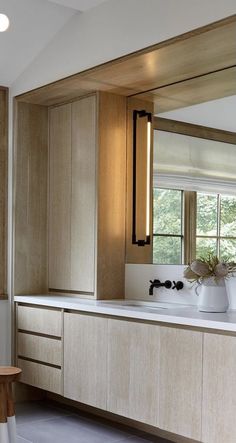 a kitchen with wooden cabinets and white counter tops in front of a large mirror on the wall