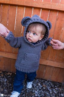 a small child wearing a knitted bear hoodie with his hands in the air