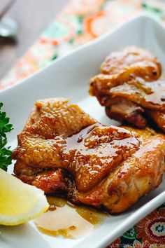 two pieces of meat on a white plate with lemon wedges and parsley next to it