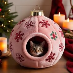 a cat in a pink ball shaped bed with snowflakes on it and candles